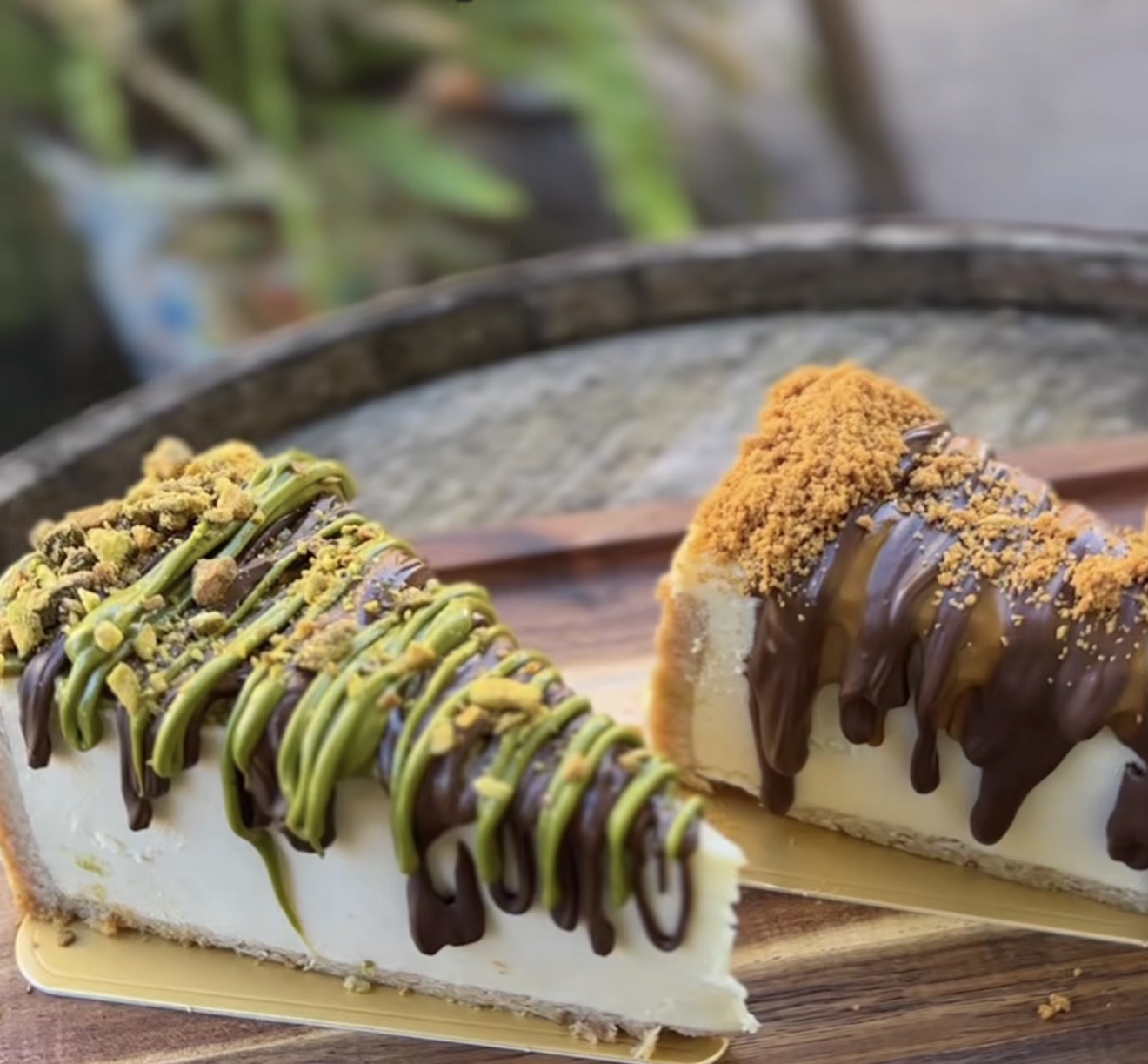 Two cheesecake slices side by side — pistachio and Biscoff, both finished with drizzle and crumb